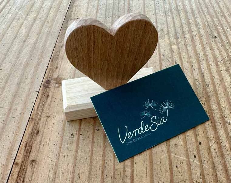 VerdeSia, Die Bestatterin in Peiting Kleines Holzherz auf einem Tisch mit angelehnter Visitenkarte des Unternehmens VerdeSia
